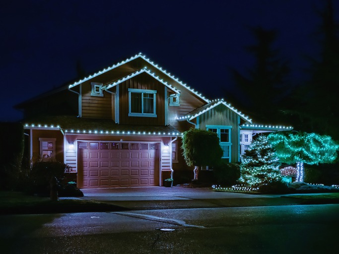 A house is adorned with festive white lights, illuminating its exterior and surrounding trees at night, creating a warm, inviting atmosphere.