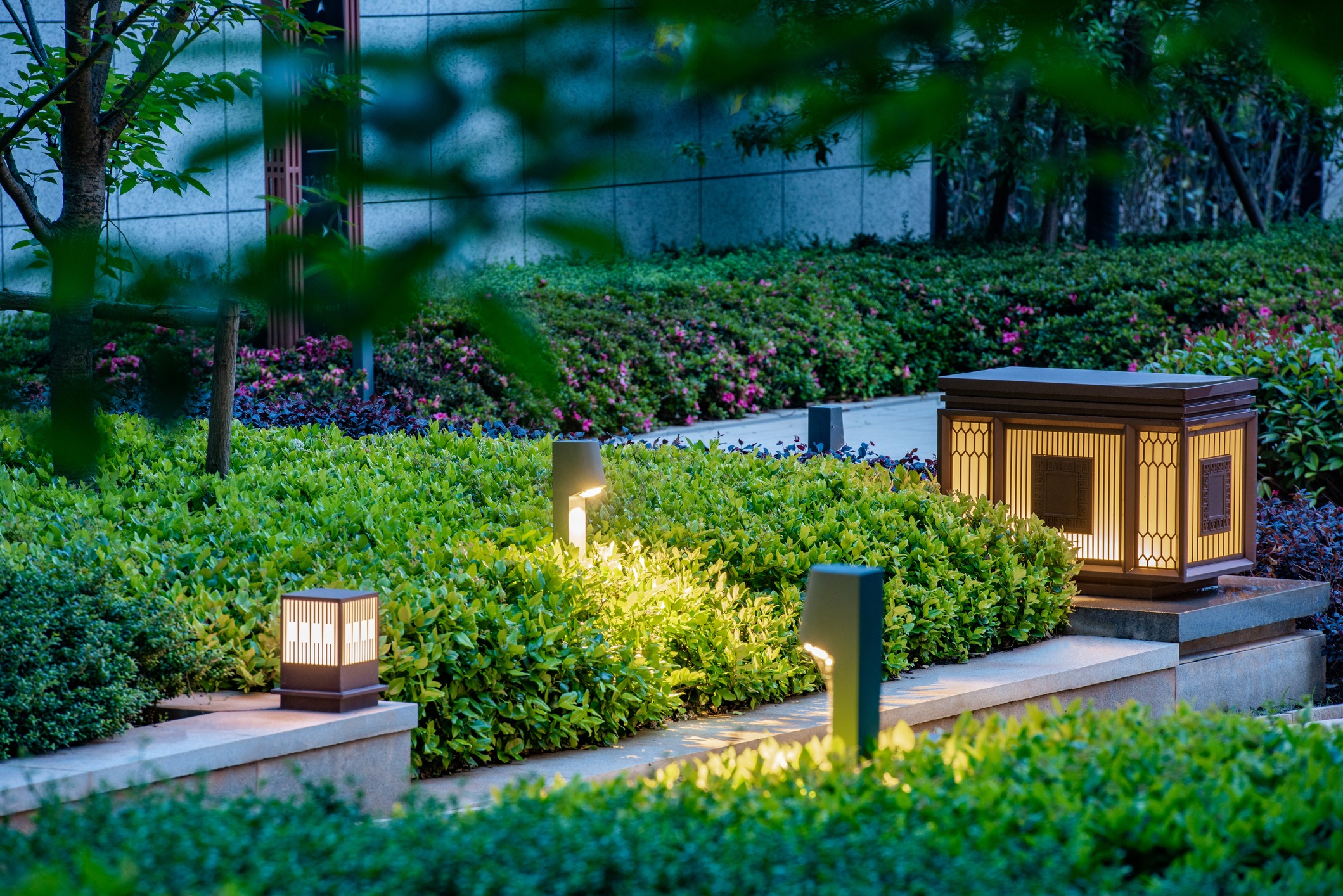Garden with neatly trimmed bushes and subtle lighting from decorative lanterns, creating a serene and peaceful atmosphere amidst greenery.