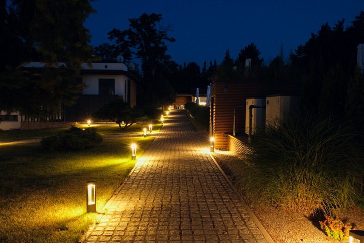 A cobblestone path illuminated by streetlights at night, lined with modern buildings and trees in a quiet, residential area.