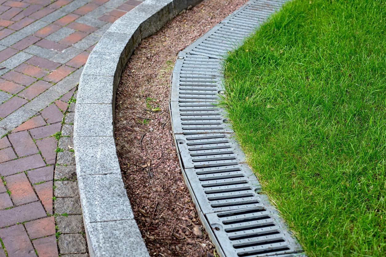 Curved pathway with brick and stone edging, alongside green grass and metal drainage cover, creating a neat and organized outdoor space.