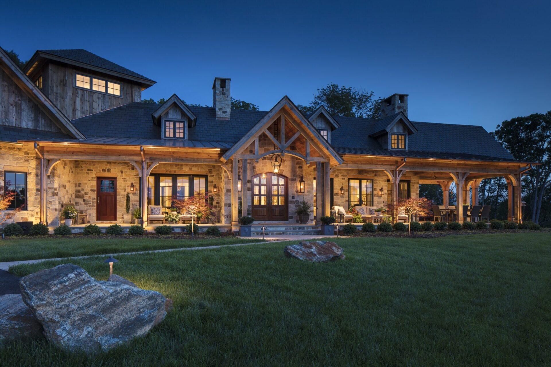modern rustic home with landscape lighting highlighting stone walls, wooden beams, and outdoor seating areas at dusk