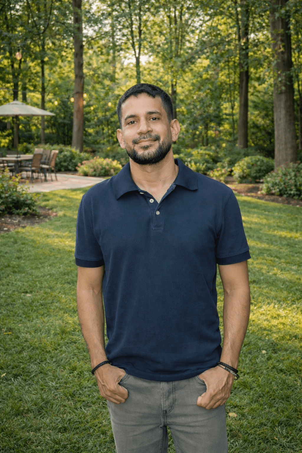 A person in a navy shirt stands in a lush, green backyard with patio furniture and tall trees in the background.
